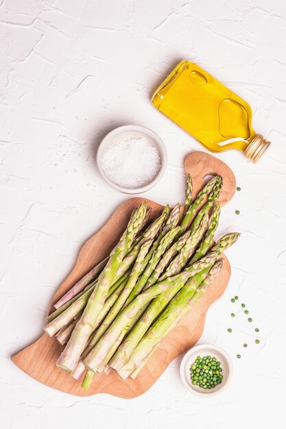 Espárragos maduros sobre una tabla de cortar de madera. Ingredientes frescos listos para cocinar alimentos saludables. Luz dura moderna, sombra oscura. Fondo de masilla blanca, vista superior