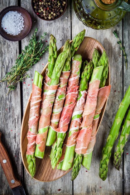 Espárragos orgánicos frescos envueltos en prosciutto en una vista superior de la tabla de cortar