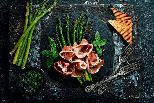 Espárragos a la parrilla con prosciutto y albahaca Sobre un fondo de piedra negra Vista superior