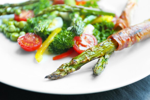 Espárragos a la parrilla con tocino y verduras en plato