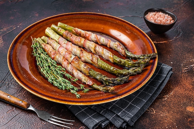 Espárragos verdes asados envueltos con tocino en un plato. Fondo oscuro. Vista superior.