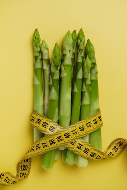 Foto espárragos verdes y cinta métrica aislados en amarillo