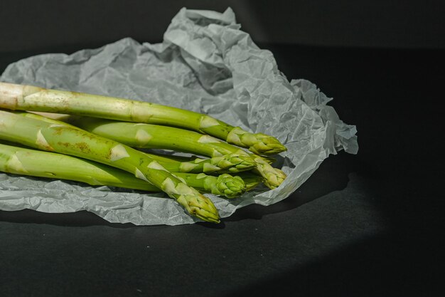 Los espárragos verdes frescos se encuentran sobre un pergamino blanco sobre un fondo gris oscuro nutrición adecuada Lugar de estilo de vida para el texto