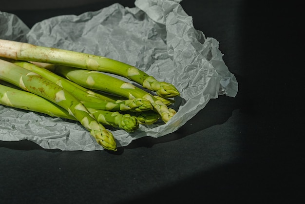 Los espárragos verdes frescos se encuentran sobre un pergamino blanco sobre un fondo gris oscuro nutrición adecuada Lugar de estilo de vida para el texto