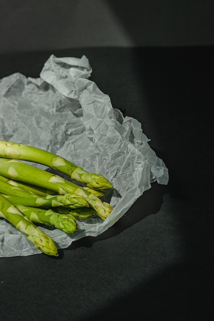 Los espárragos verdes frescos se encuentran sobre un pergamino blanco sobre un fondo gris oscuro nutrición adecuada Lugar de estilo de vida para el texto