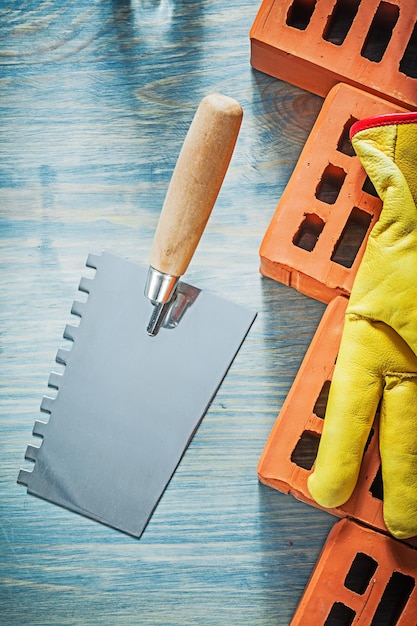 Espátula guantes de seguridad de ladrillos rojos en concepto de albañilería de tablero de madera.