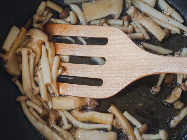 Espátula de madera de primer plano con champiñones en rodajas salteados en sartén negra, comida casera