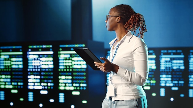 Especialista afroamericano paseando por las filas de servidores que proporcionan recursos de procesamiento para diferentes cargas de trabajo. Mujer experimentada monitoreando supercomputadoras encargadas de resolver operaciones complejas