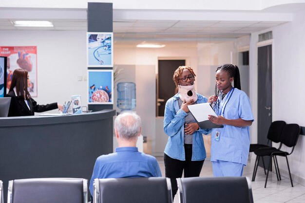 Especialista americano africano e pessoa fazendo check-up no saguão da sala de espera, usando colar cervical após lesão por acidente. Assistente médico que consulta a mulher ferida no centro de saúde.