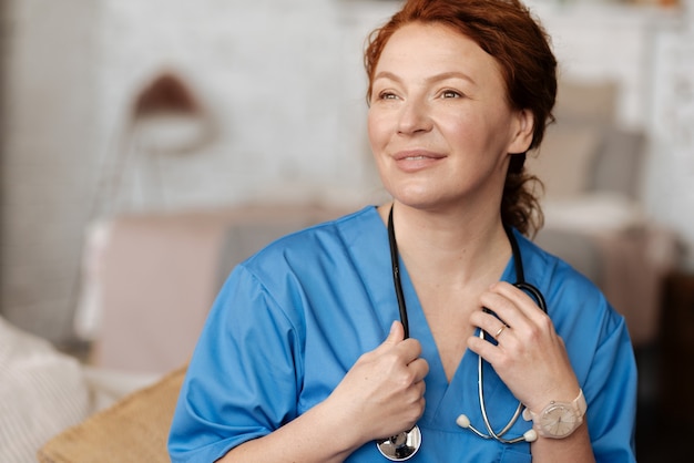 Especialista avançado. linda médica treinada esperando por uma consulta, segurando seu estetoscópio e vestindo um uniforme especial