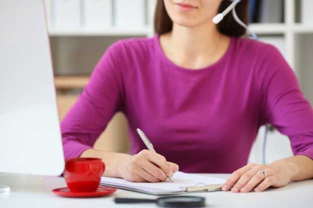 Una especialista en call center toma pedidos por teléfono y los escribe en un cuaderno, con una imagen de profundidad de campo