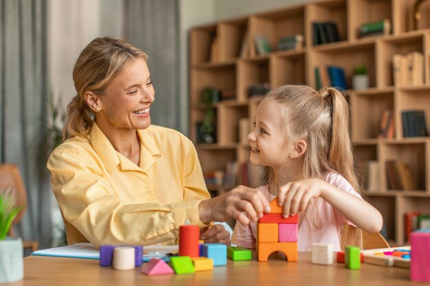 Especialista em desenvolvimento infantil amigável tendo sessão com garotinha brincando com tijolos de madeira coloridos