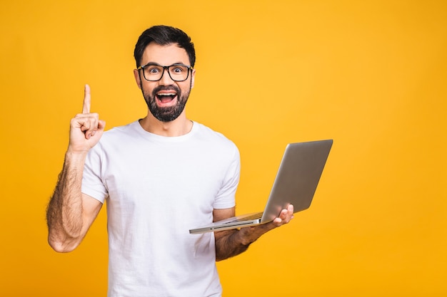 Especialista em negócios confiável. Confiante jovem bonito barbudo homem casual segurando laptop e sorrindo em pé sobre fundo amarelo isolado.