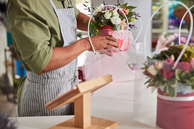 Especialista floral vestindo um avental e camisa marrom deixando um vaso com flores em um pacote transparente