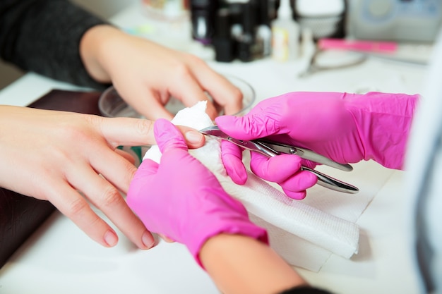 Foto especialista en manicura en el cuidado de los guantes de goma con la uña en el salón de belleza del spa. el manicurista utiliza una herramienta de manicura profesional. servicio de manicura.