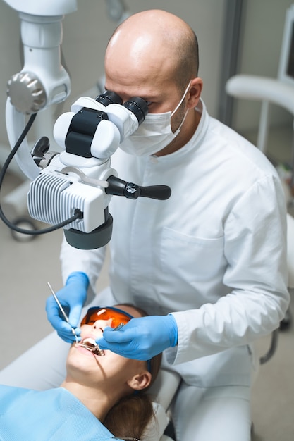 Especialista masculino está usando ferramentas e máquina eletrônica moderna para tratar o paciente na cadeira odontológica