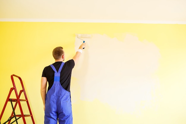 Especialista masculino pinta la pared con pintura en interiores, concepto de reparación