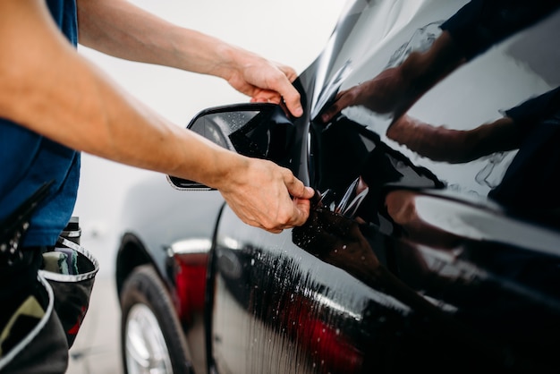 Especialista masculino trabalha com carro, processo de instalação de filme colorido, procedimento de instalação de vidro automotivo colorido