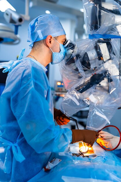 Especialista médico que realiza cirugía con equipo moderno Perfil de cirujano en máscara mirando al microscopio en el quirófano