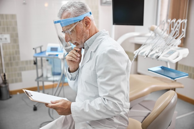 Especialista odontológico idoso focado usando um visor e olhando para a lista de consultas