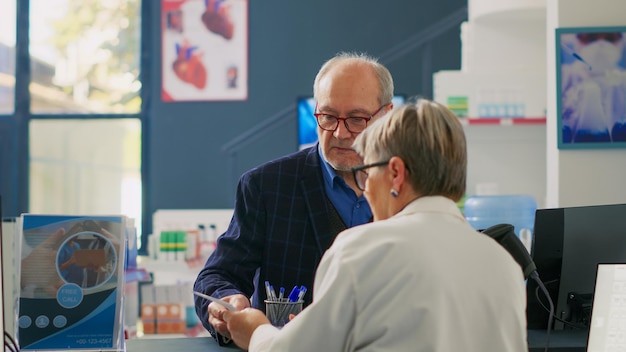 Especialista en salud ayudando a clientes mayores con papel de prescripción, encontrando píldoras y suplementos para el tratamiento de enfermedades. Anciano buscando medicamentos en el mostrador de la farmacia, caja registradora.