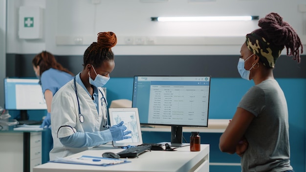 Especialista sosteniendo una tableta con huesos para una visita de revisión ortopédica, mostrando la anatomía del esqueleto humano a un paciente joven. Médico señalando la figura de la osteopatía en el dispositivo para el diagnóstico sanitario.