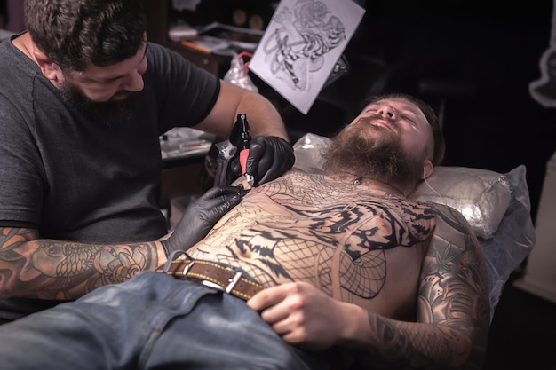 El especialista en tatuajes hace un tatuaje en un salón de tatuajes.