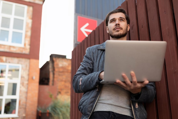 Especialista en TI trabajando en una computadora portátil apoyada contra la pared exterior