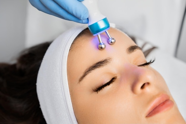El especialista utiliza un dispositivo de masaje de microcorrientes en la frente de la mujer para eliminar las arrugas