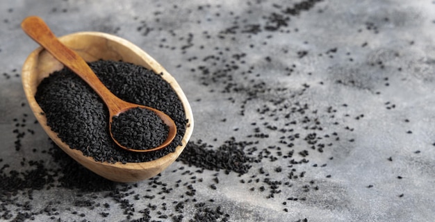 Especiaria indiana Cominho preto nigella sativa ou sementes de kalonji em tigela com colher na mesa de madeira fechar