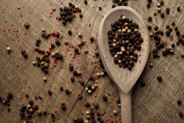 Especiarias de cravo-da-índia de sal marinho de ervilhas de pimenta preta e branca em uma colher em um fundo de madeira