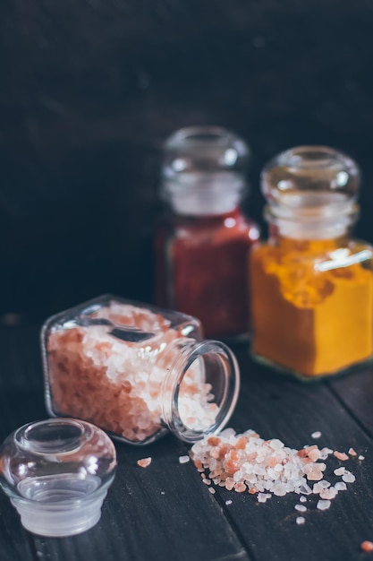 Foto especias aromáticas brillantes en frascos de vidrio, surtidos de especias: sal rosa, paprika y cúrcuma sobre fondo de piedra negra.