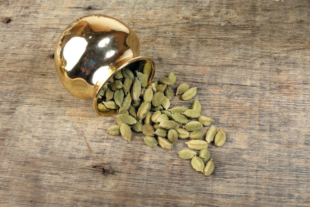 Especias de cardamomo en una olla de metal dorado sobre madera rústica