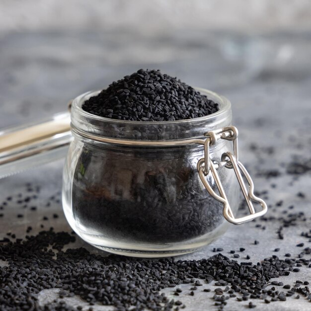 Especias indias Comino negro nigella sativa o semillas de kalonji frasco de vidrio sobre mesa gris de cerca Medicina asiática tradicional concepto de comida saludable y vegetariana