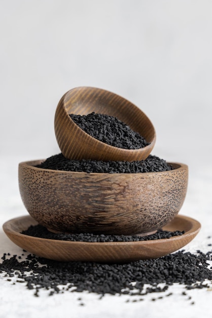 Especias indias Semillas de comino negro nigella sativa o kalonji en cuencos de madera sobre mesa blanca de cerca Medicina tradicional concepto de comida saludable y vegetariana