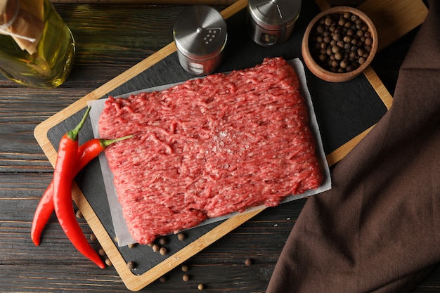 Especias y tabla de cortar con carne picada en madera, vista superior