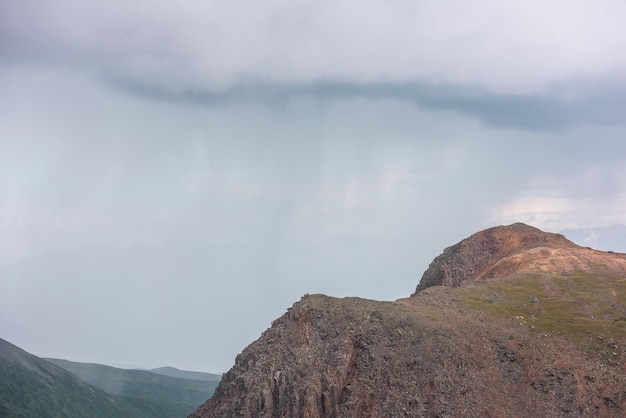 Espectacular paisaje aéreo con la cima de la montaña iluminada por el sol durante la lluvia en un clima cambiante Paisaje atmosférico de montaña con rocas afiladas a la luz del sol bajo un cielo nublado gris plomo Nubes lluviosas en las montañas