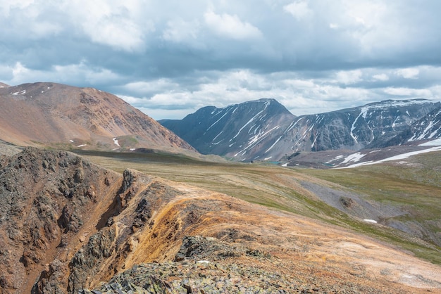 Espectacular paisaje alpino con abismo y alta cordillera a la luz del sol bajo un cielo nublado Paisaje colorido con rocas afiladas iluminadas por el sol cerca del borde del precipicio y una gran cordillera en un clima cambiante