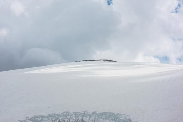 Espectacular paisaje alpino con enorme cúpula de montaña nevada con cima rocosa a la luz del sol bajo un cielo nublado gris Impresionante paisaje de montaña con alta montaña nevada en forma de cúpula en el centro en un clima cambiante