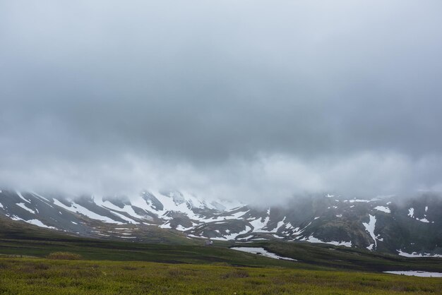 Espectacular paisaje alpino con montañas nevadas en nubes bajas grises. Paisaje atmosférico sombrío de tundra bajo el cielo gris plomo. Vista sombría y minimalista a la cordillera entre nubes bajas y lluviosas en cielo nublado.