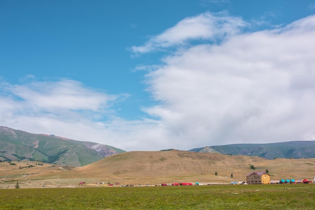 Espectacular paisaje alpino con pequeñas casas en una pradera verde iluminada por el sol contra una gran colina bajo las nubes en el cielo azul Hermoso paisaje montañoso con un clima cambiante Vista panorámica a la alta cordillera