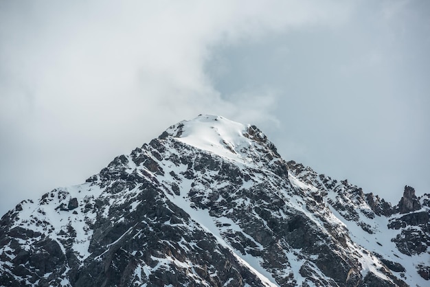 Espectacular paisaje con la cima de una alta montaña nevada iluminada por el sol en un cielo nublado Nieve blanca sobre rocas negras en el cielo nublado Impresionante pico de montaña nevado a la luz del sol en un clima cambiante Montaña nevada en las nubes