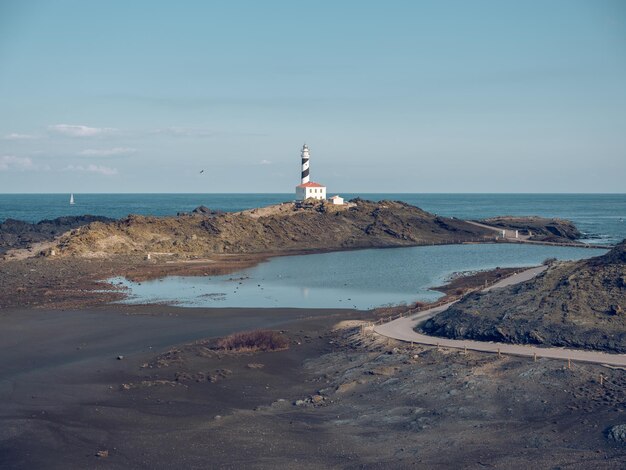 Espectacular paisaje del faro situado en la costa con rocas bañadas por tranquilas aguas azules del mar en un día soleado