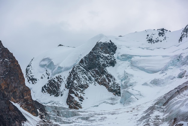 Espectacular paisaje con gran cima de montaña nevada con cornisa de hielo y glaciar bajo un cielo gris nublado Gran glaciar con cascada de hielo a gran altura Paisaje sombrío en montañas nevadas en primer plano nublado