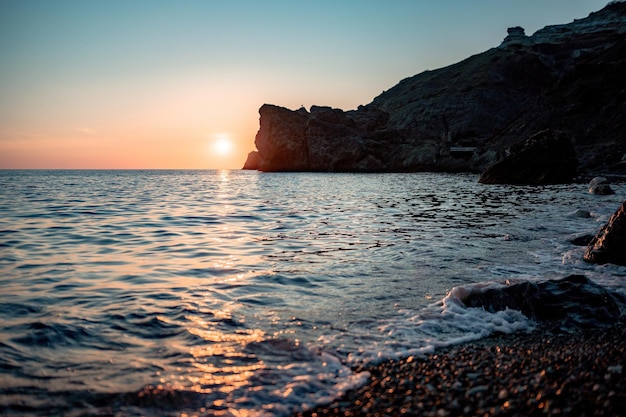 El espectacular paisaje marino sobre la playa durante la puesta de sol con acantilados volcánicos rocosos está iluminado por la cálida puesta de sol