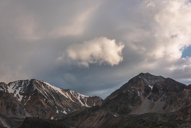 Espectacular paisaje de montaña con alta cordillera con un pináculo rocoso afilado bajo nubes de color puesta de sol en un cielo sombrío Paisaje atmosférico oscuro con grandes montañas con nieve en un clima cambiante