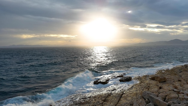 Espectacular puesta de sol sobre el mar después de la tormenta, fuertes olas rompen en la costa rocosa.