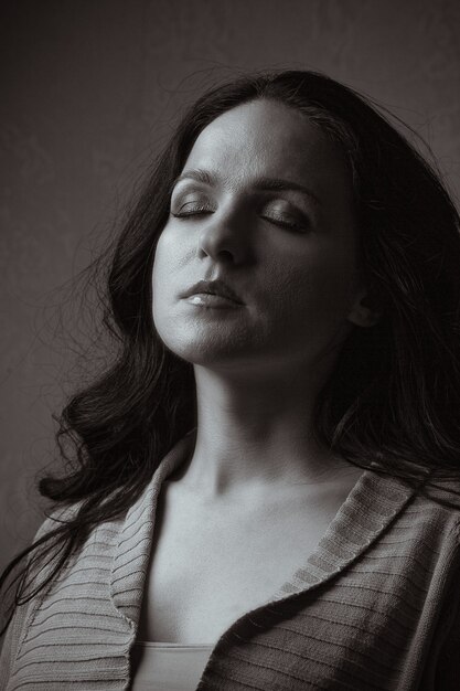 Espectacular retrato de mujer impresionante con cabello largo y ojos cerrados posando en la sombra. Tono monocromo