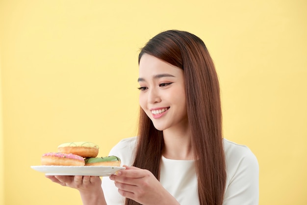 Espectáculo de chicas asiáticas y sosteniendo un plato lleno de deliciosos donuts aromáticos deliciosos en la cara de la sonrisa aislada.