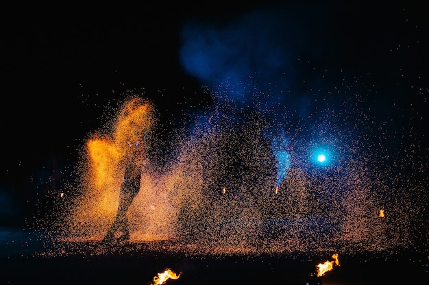 Espectáculo de fuego, baile con llamas, maestro masculino haciendo malabares con fuegos artificiales, actuación al aire libre, dibuja una figura ardiente en la oscuridad, chispas brillantes en la noche. Un hombre con un traje LED baila con fuego.